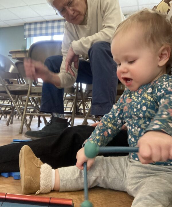 Young child plays colorful percussion instruments with mallets as an adult plays along.
