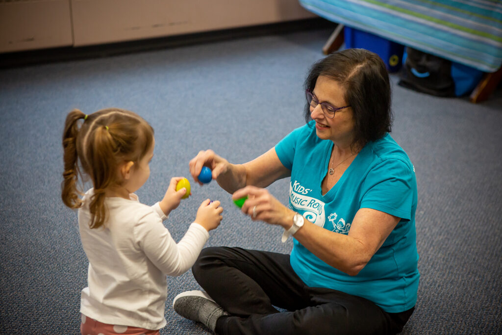 Music teacher and young child explore colorful egg shakers together.