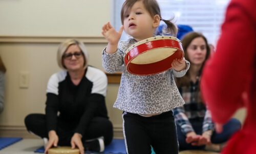 Young child moves while holding a red tambourine during a music and movement class.