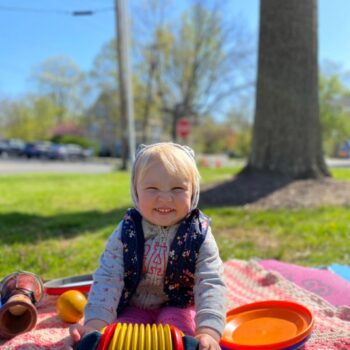Child sitting on a mat playing a variety of instruments during an outdoor music and movement class.